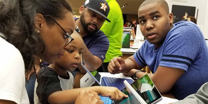 child points at a laptop screen while three older people look on