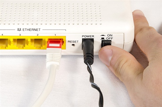 person's thumb pushing an on and off switch on a router