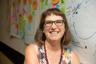 Beth Kanter sitting next to a wall with large sheets of paper and sticky notes