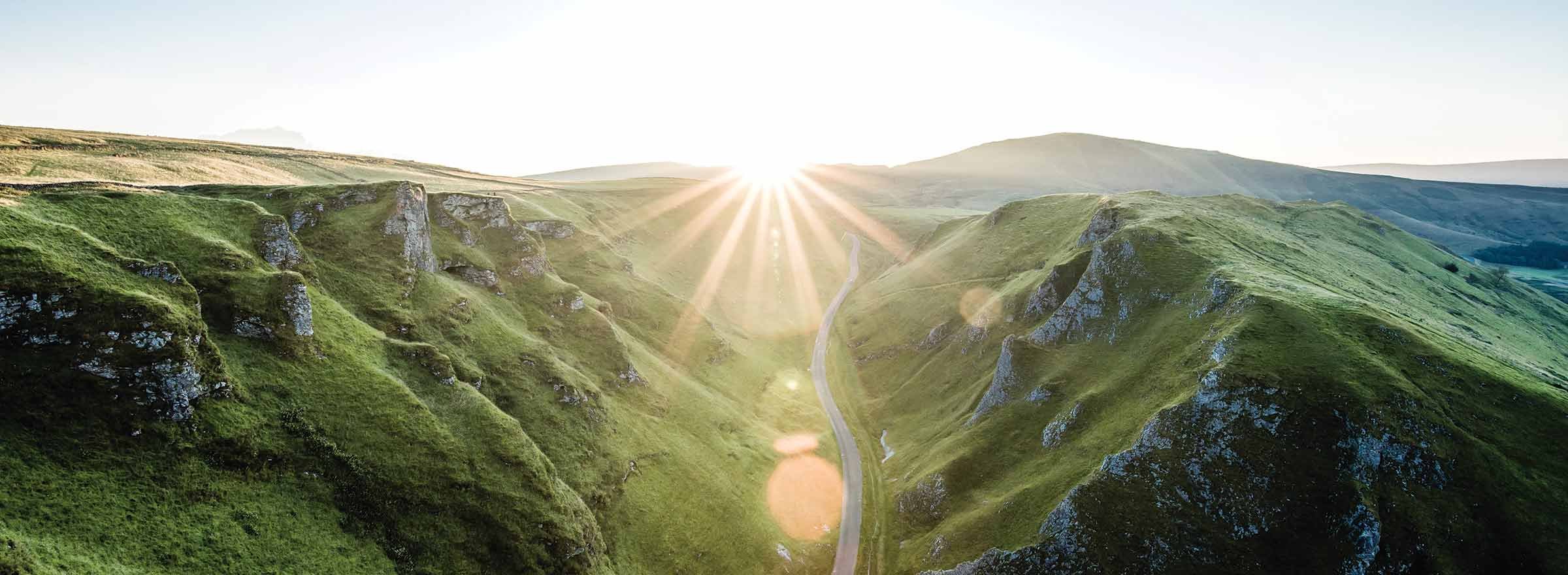 sunlight shining on a road that leads between grassy hillsides, representing the benefits to the environment of the TechSoup Refurbished Hardware Program
