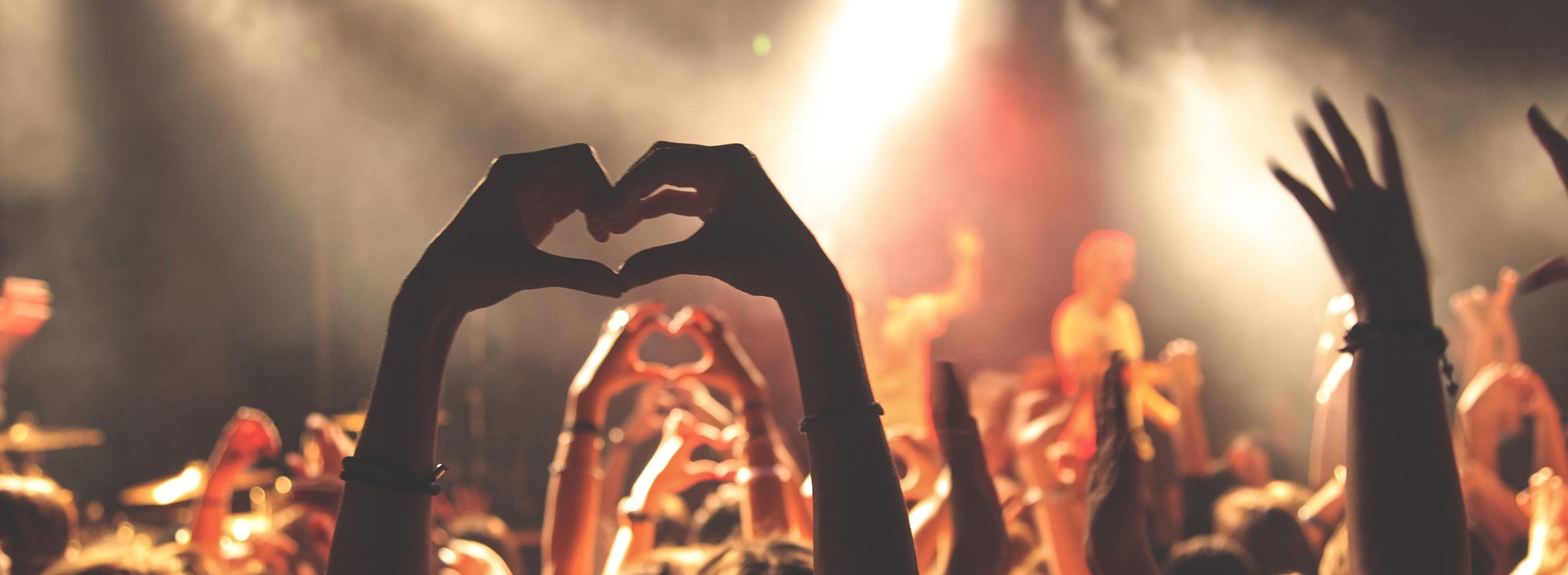 people at a concert holding up their hands in the shape of a heart, representing millennials and their potential to support nonprofit causes and fundraising