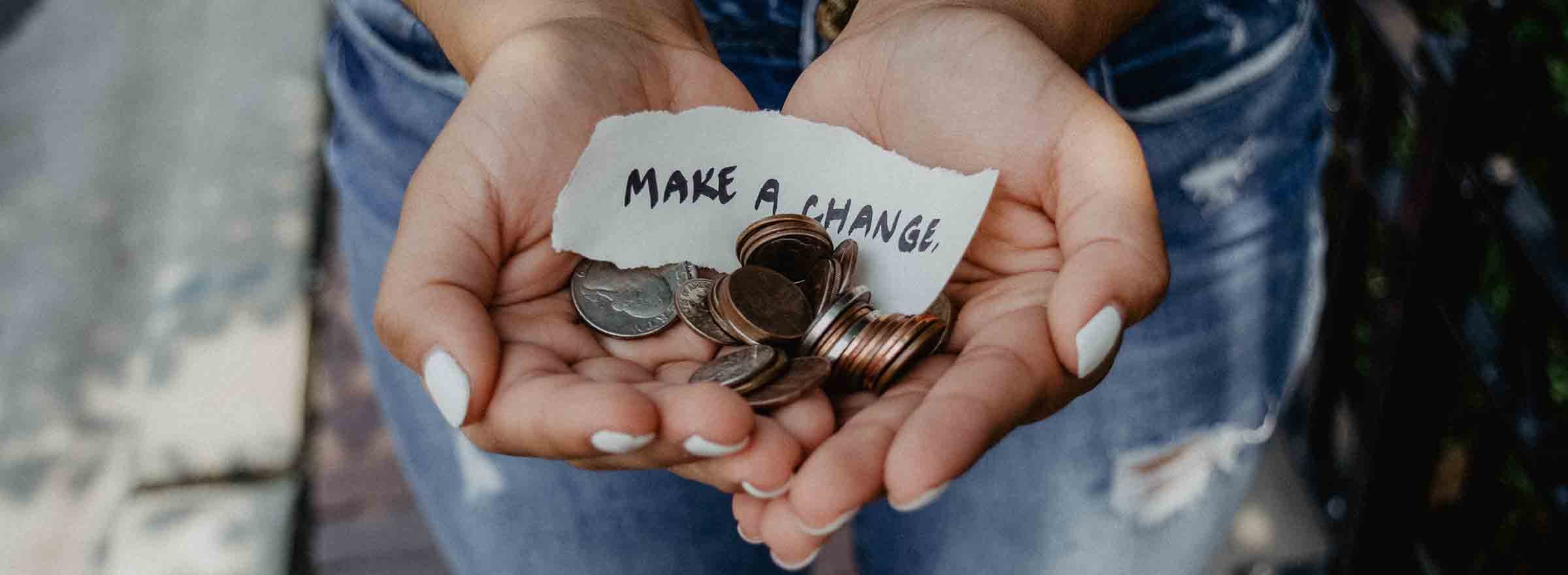 hands holding coins and a piece of paper that says make a change, representing the promise of monthly giving for nonprofit fundraising