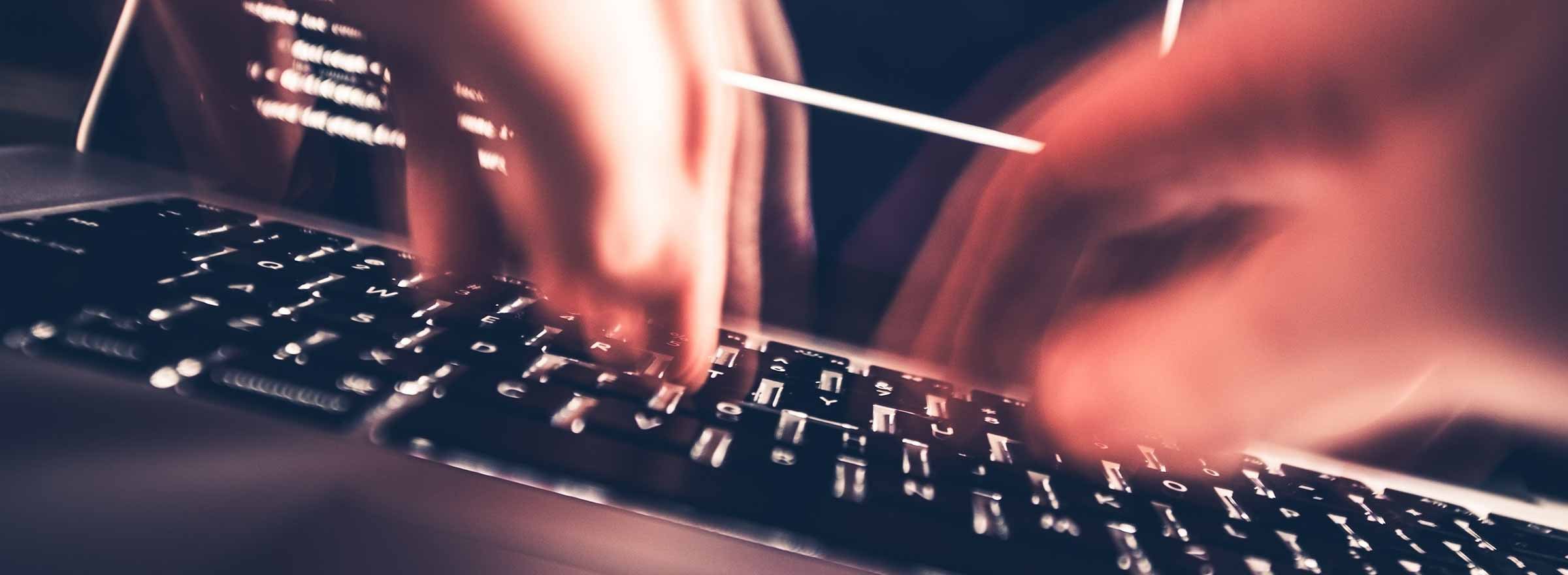blurry photo of hands typing on a laptop keyboard