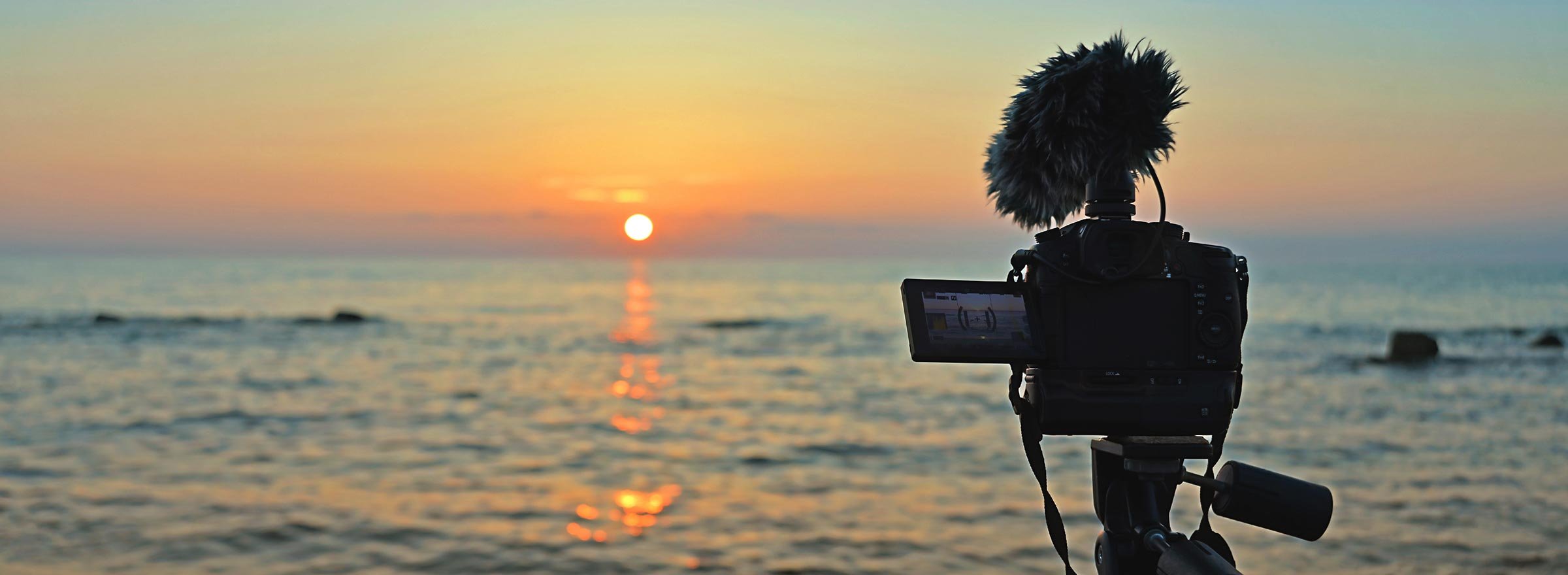 camera on tripod and supporting microphone points over the water to a setting or rising sun