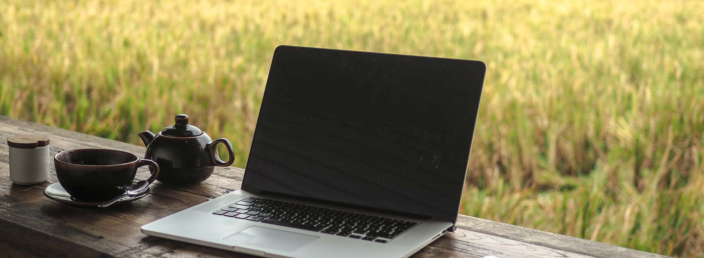 laptop on an outdoor table with a teapot and cup