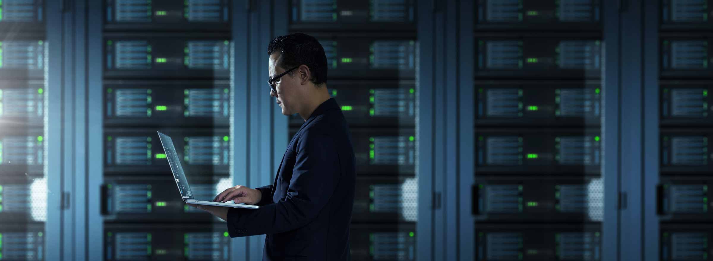 man standing in a datacenter and holding a laptop