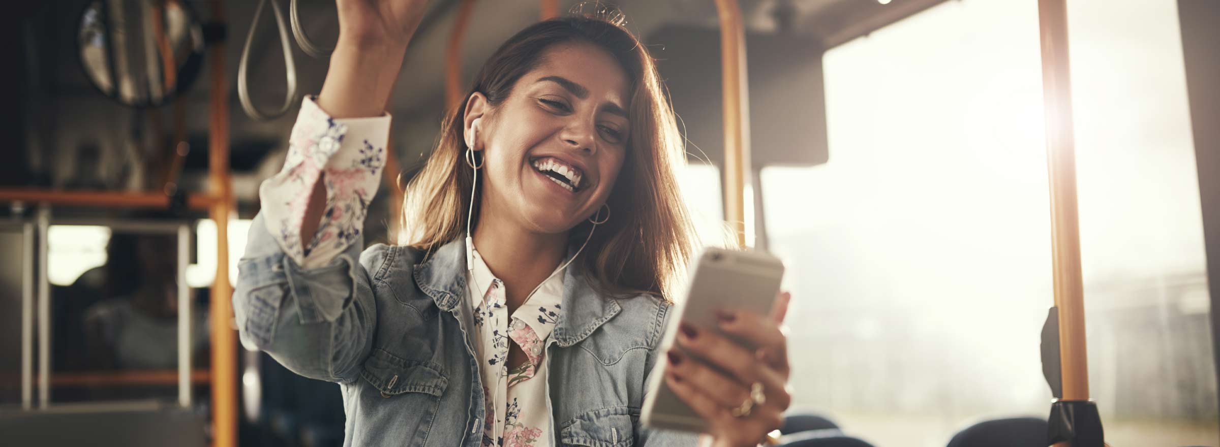 young woman standing on public transit looking at a smartphone and smiling