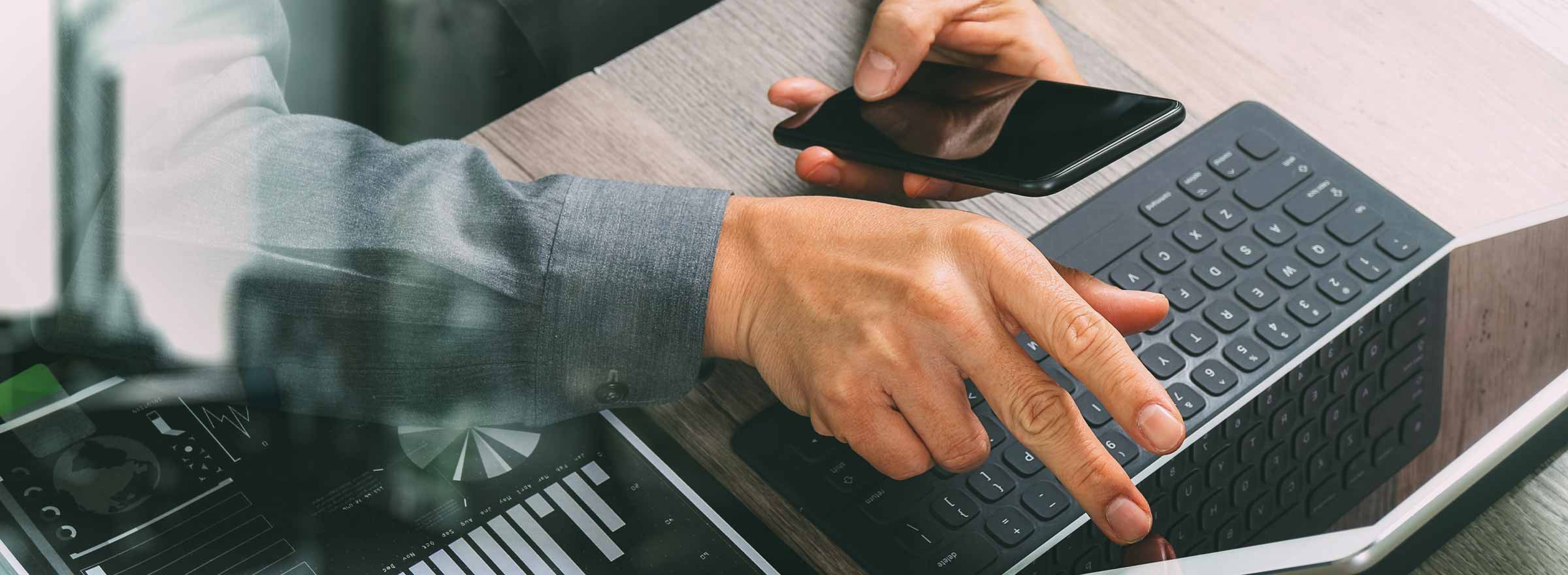 hands of a man using both a smartphone and a laptop