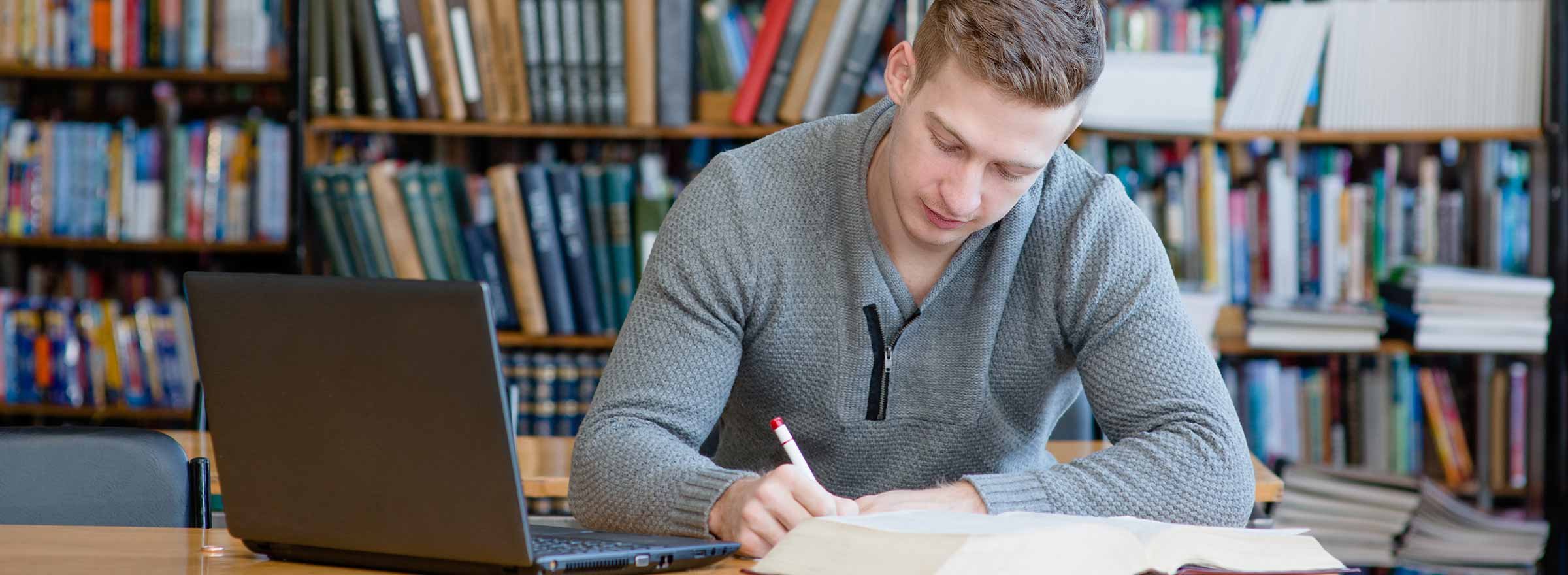 man in library using paper notes and a laptop
