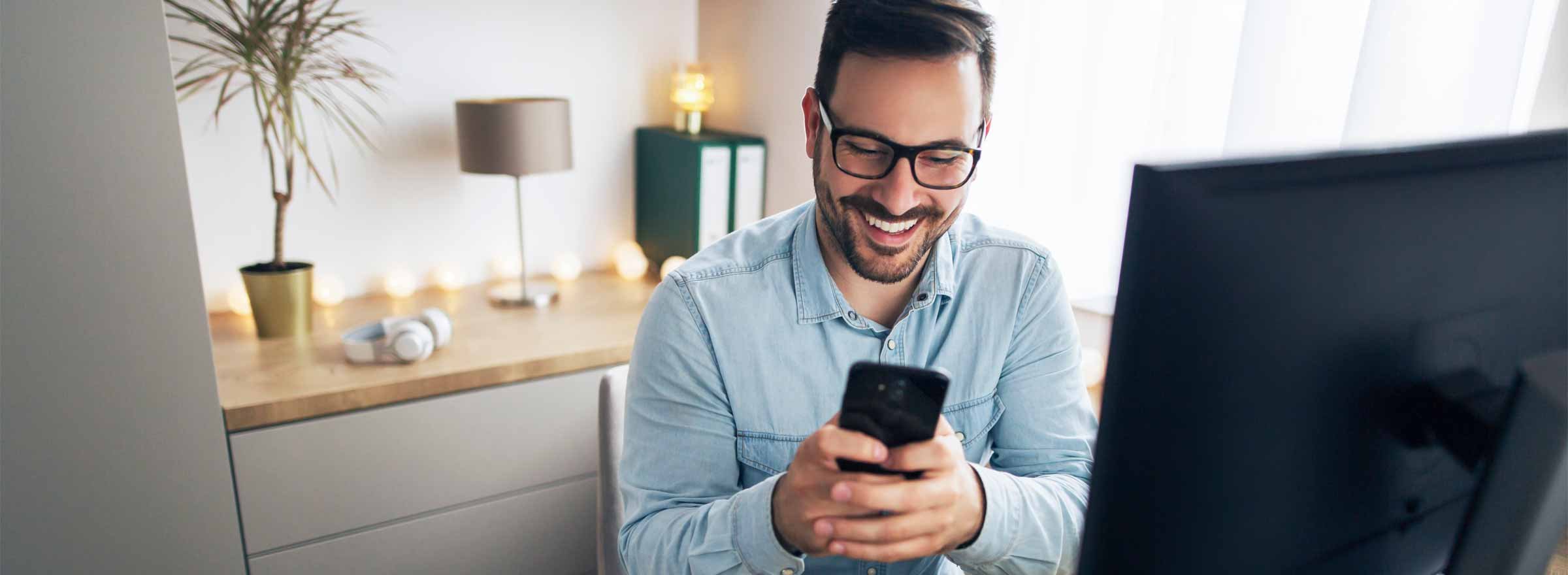 man sitting at a computer and smiling at a smartphone