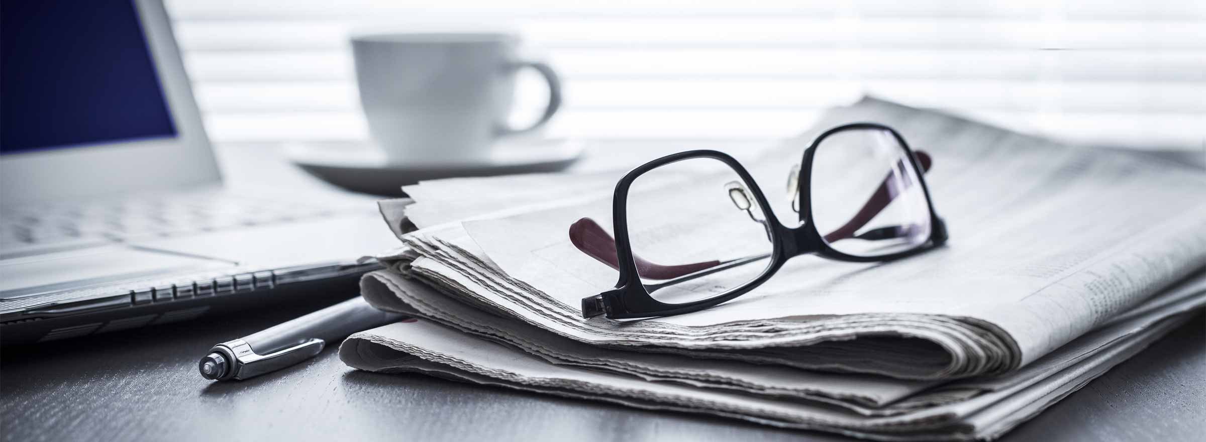 eyeglasses resting on a newspaper in front of a computer