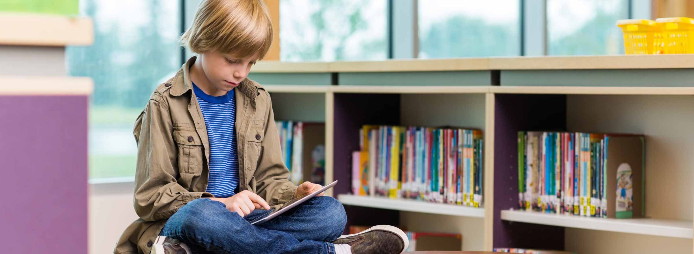 boy sitting on the floor in a library using a tablet