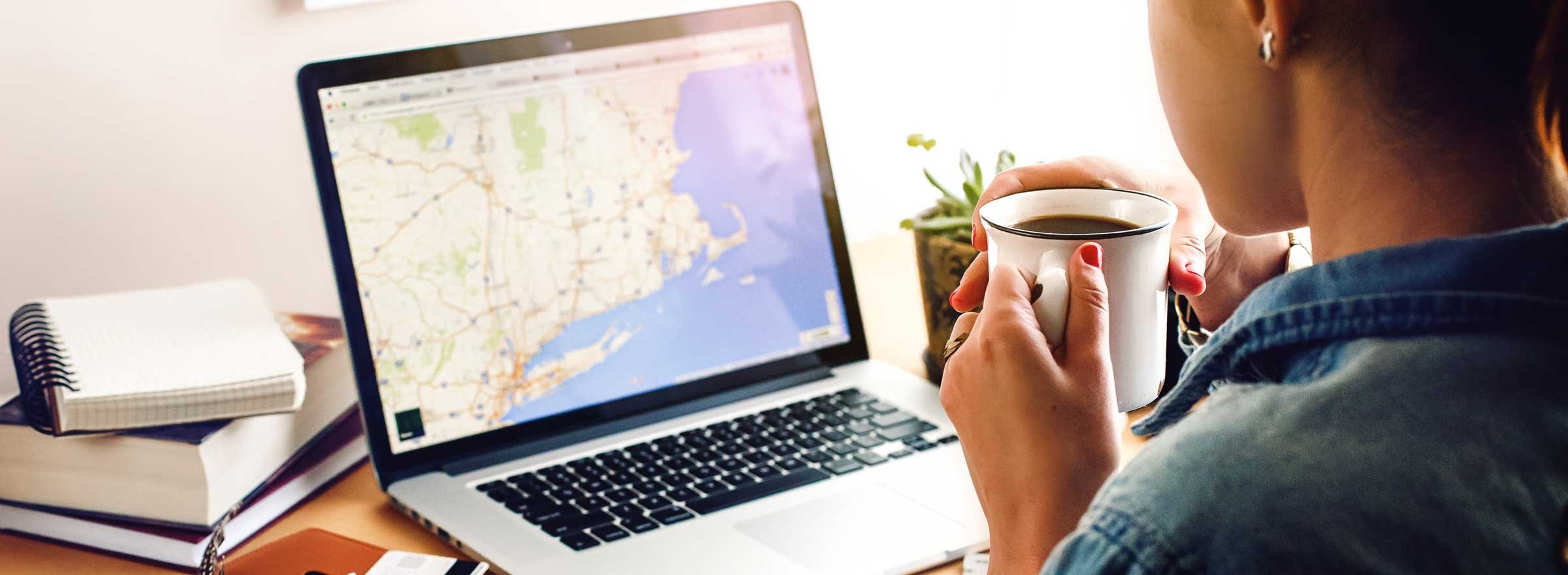 woman drinking coffee and looking at a map of the northeast US on a computer screen
