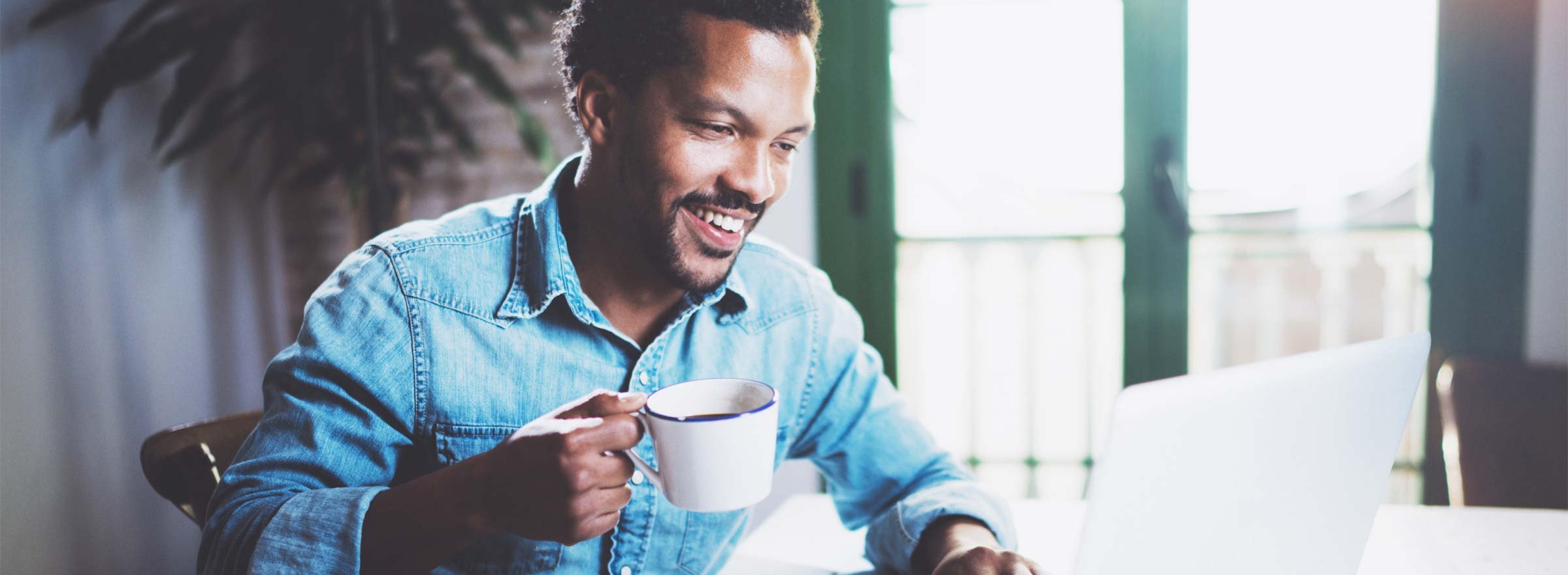 man drinking coffee and smiling at a computer