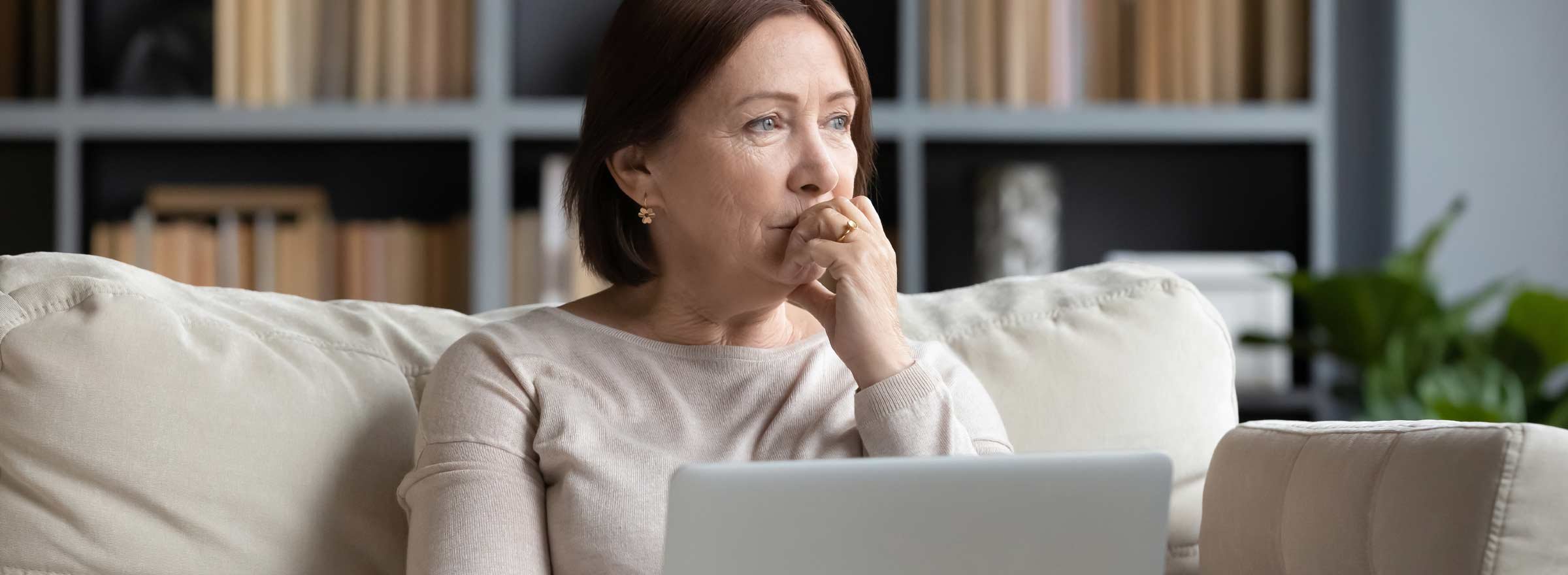 woman on a sofa holding a laptop and gazing into the distance