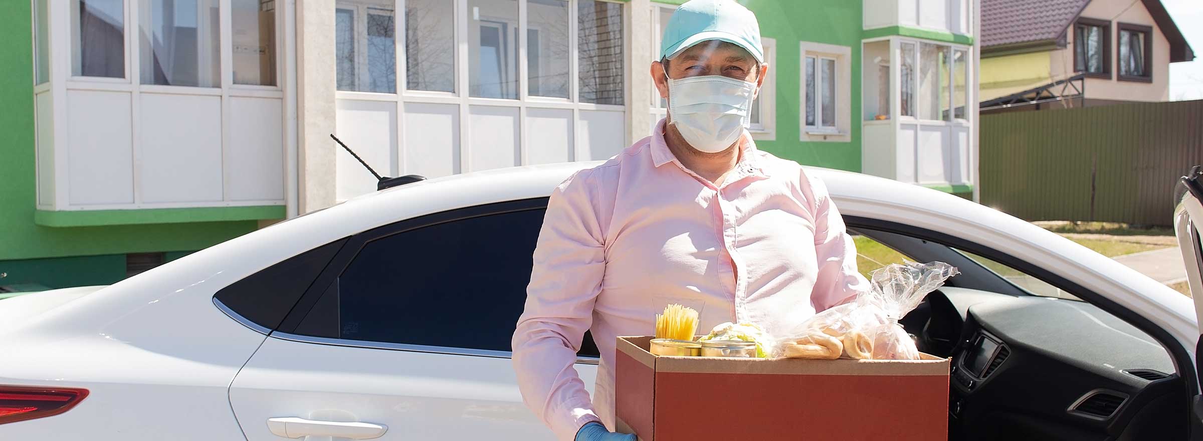 man in a face mask carrying a box of food in a residential neighborhood
