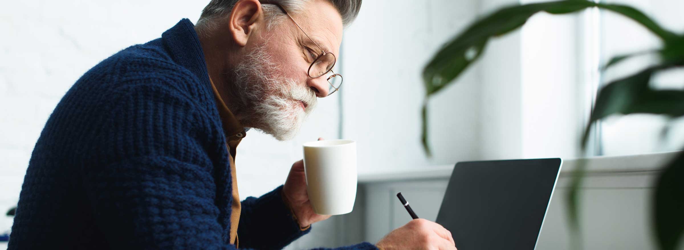 man at a computer holding a mug and a pencil