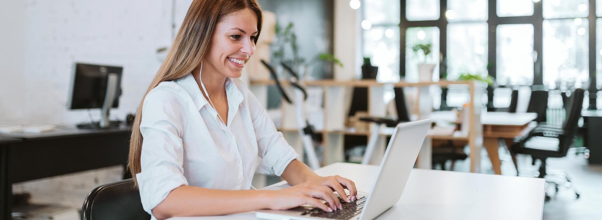 woman in office typing on a laptop and wearing earbuds