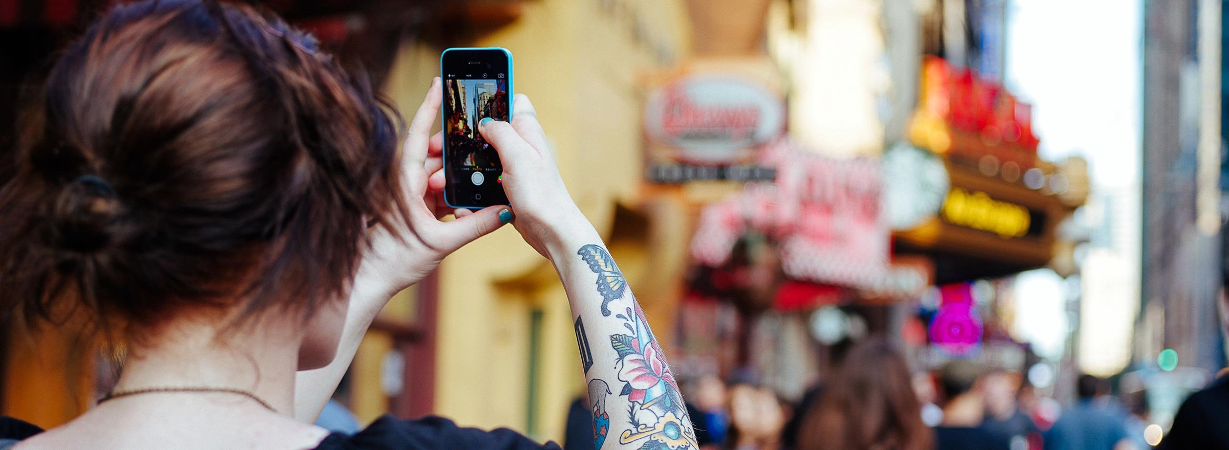 woman with a tattooed arm taking a picture with her cellphone