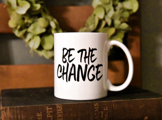 white mug with black lettering saying be the change