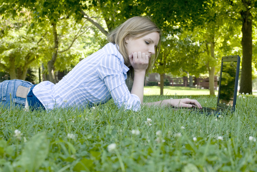 girl lying in wildflower field looking at laptop